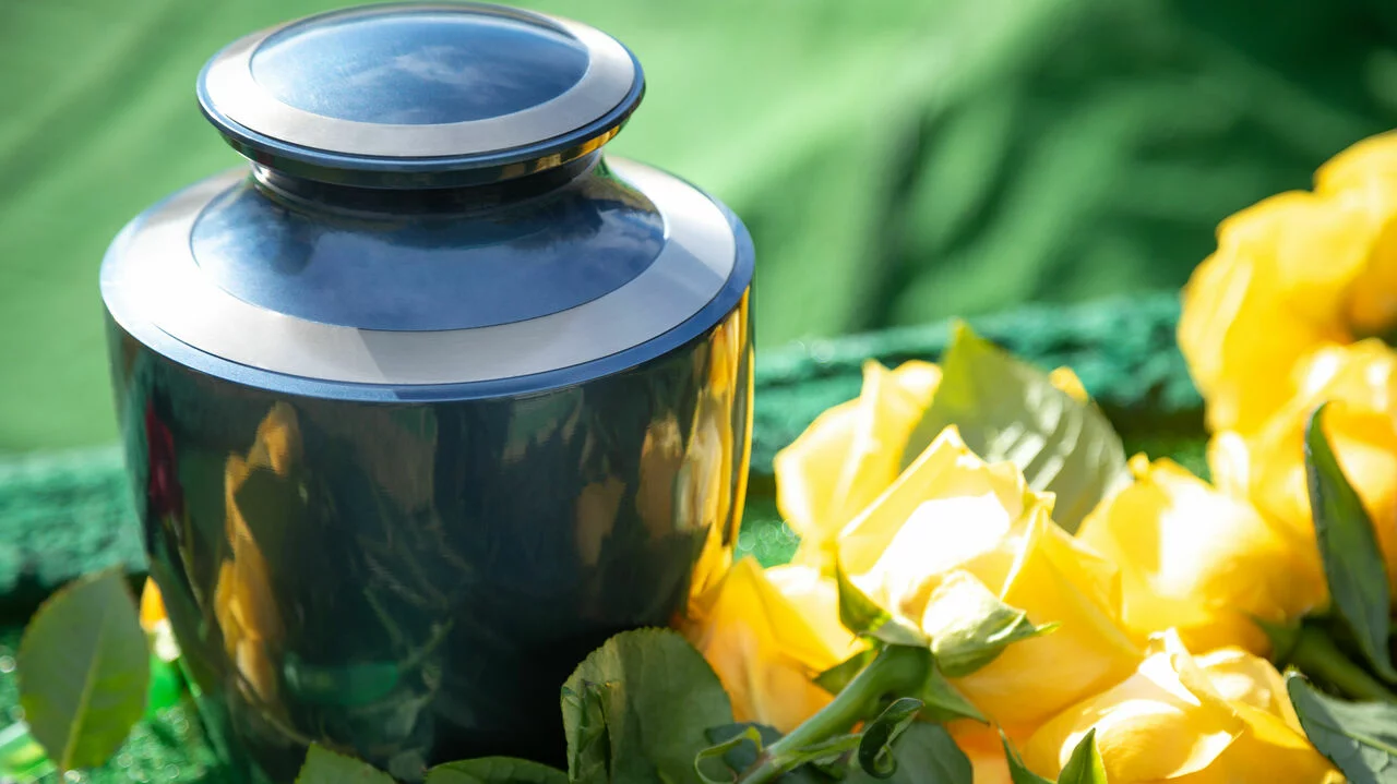 Dunkle Urne mit gelben Rosen steht an einem Urnengrab